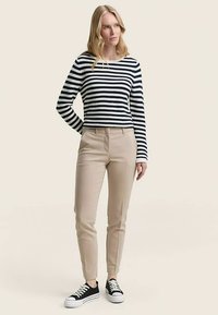 Chemise à manches longues rayée bleu marine et blanc, pantalon beige ajusté, et baskets noires. Tissu lisse, coupe cintrée, et motifs classiques.