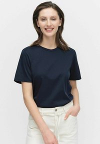 Marinblå bomulls-t-shirt med kort ärm, rund halsringning, slät textur, kombinerad med vita högmidjade byxor.