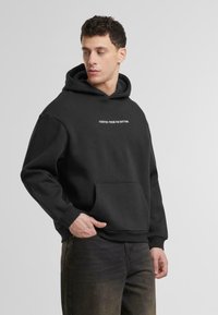 Svart het hoodie gjord av mjukt tyg. Har en framficka och vit text "STARTADE FRÅN BOTTNEN" över bröstet.