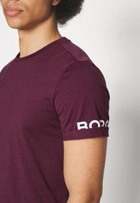 Kortärmad burgundy T-shirt i mjukt tyg. Funktioner vit text "BORO" på ärmen, figurnära design och rund halsringning.