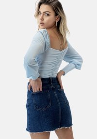 Lysblå, tætsiddende top med rynkedetalje og lange ærmer; parret med en mørk denim mini skirt med frynset kant og baglommer.