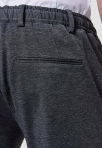 Grey athletic sweatpants made from a textured fabric, featuring an elastic waistband and a discreet back pocket with a contrasting zipper.
