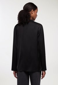Maglietta nera a maniche lunghe in tessuto leggero e liscio, con scollatura rotonda e vestibilità rilassata. Presenta un dettaglio di cucitura minimale sull'orlo.