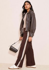 Brun läderbomberjacka, beige topp, bruna vida byxor med vit rand och vita sneakers; svart handväska med lång rem.