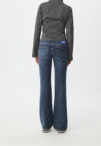 Striped black and white long-sleeve shirt paired with blue high-waisted flared jeans, featuring a contrasting waistband logo and back pockets.