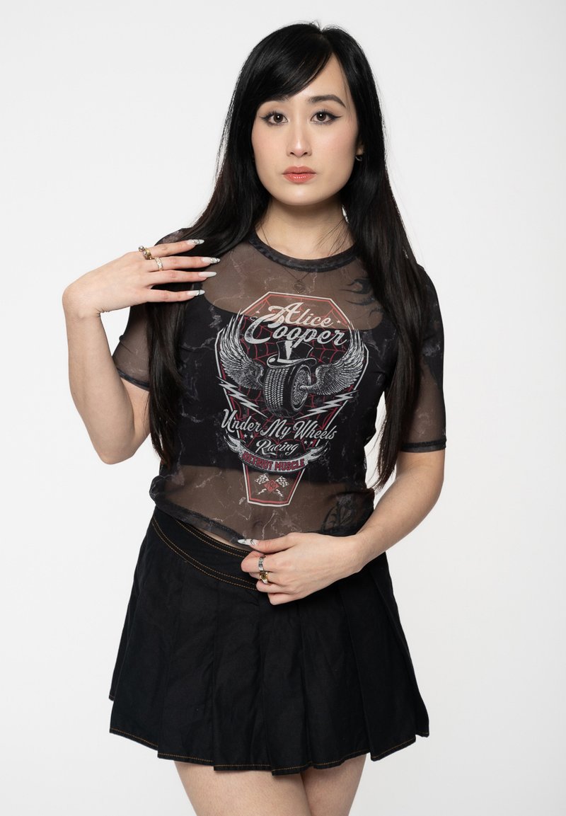 Black sheer mesh shirt with graphic print featuring the text "Alice Cooper Under My Wheels." Paired with a black pleated skirt.