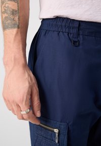 Marinen blå cargo-bukser med elastisk talje, med en lomme med lynlås i denimstruktur og en mat sølvfarvet lynlåsdetalje.
