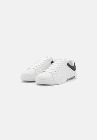 Hvite lær sneakers med svart aksent på hælen og "EXCHANGE" merking på siden. Har flate lisser og en teksturert overflate.