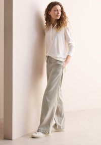 Top leggero bianco a maniche lunghe con design henley abbinato a pantaloni grigi chiari a vestibilità comoda con tasche e sneakers bianche.