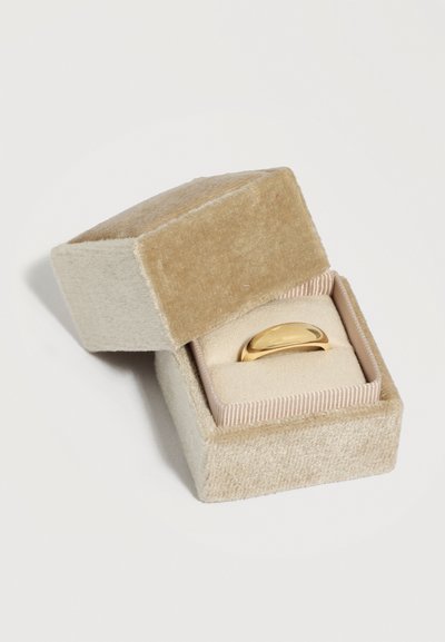 Zlatý prsteň v tvare kupoly vystavený v otvorenej béžovej zamatovej krabičke na šperky s polstrovaným vnútrom na svetlom pozadí.