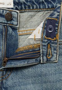 Mörkblå denimjeans med dragkedja i guldtråd, komplementär tygpatch och knappstängning. Har detaljer med fransar på den inre midjebandet.