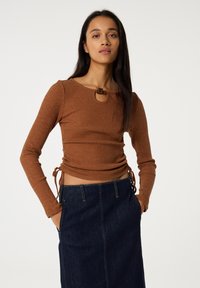 Brown ribbed long-sleeve top with a keyhole neckline and side ruching details. Paired with a dark denim skirt featuring pockets.