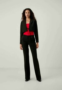 Must musta jakk punase topi peal, koos mustade kellukestega pükstega. Siledad tekstuurid ja minimalistlik disain koos sidumisaksendiga taljes.