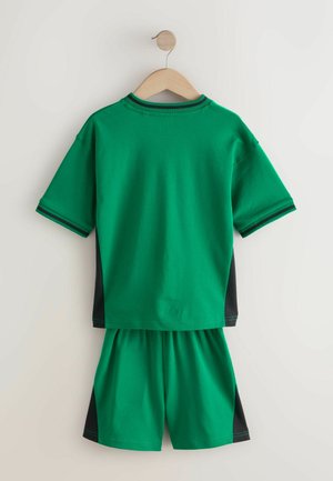 Groene katoenen sportoutfit aan een houten hanger, bestaande uit een top met korte mouwen met zwarte zijpanelen en bijpassende shorts.