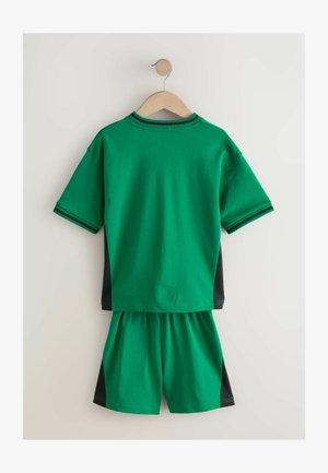 Îmbrăcăminte sport din bumbac verde pe un umeraș din lemn, având o bluză cu mânecă scurtă cu panouri laterale negre și șorturi asortate.