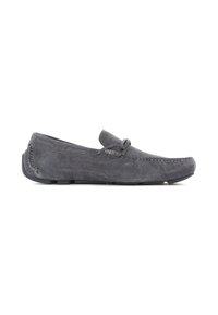 Zapato mocasín de ante gris con puntera redondeada, lazo decorativo y acentos de costura. Suela plana de goma con un ligero tacón, diseñado para la comodidad.
