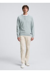 Suéter azul claro de tejido texturizado, con cuello redondo, tapeta de tres botones y puños acanalados, combinado con pantalones de color crema.