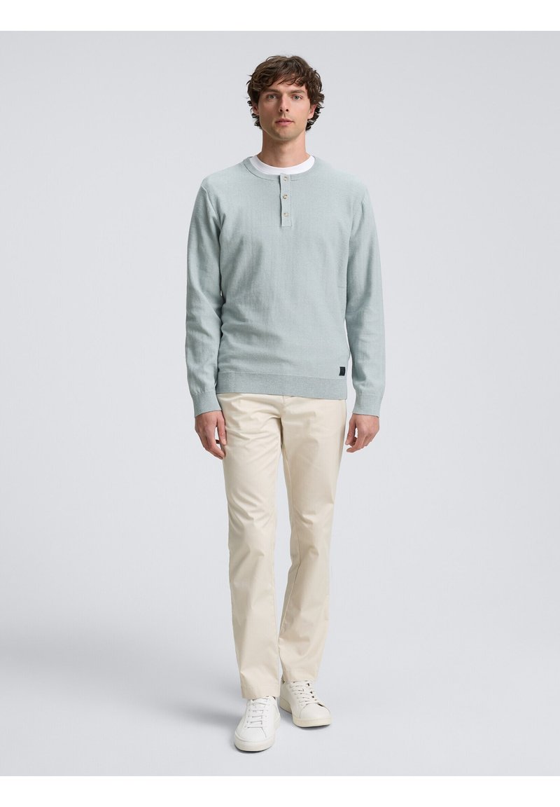 Suéter azul claro de tejido texturizado, con cuello redondo, tapeta de tres botones y puños acanalados, combinado con pantalones de color crema.
