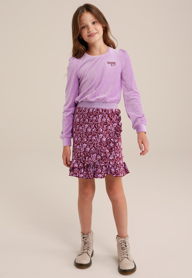 Levanduľový top s dlhým rukávom s potlačou "ADORE", kombinovaný s volánovou sukňou s kvetinovým vzorom v purpurovej farbe a béžovými čižmami na šnurovanie.