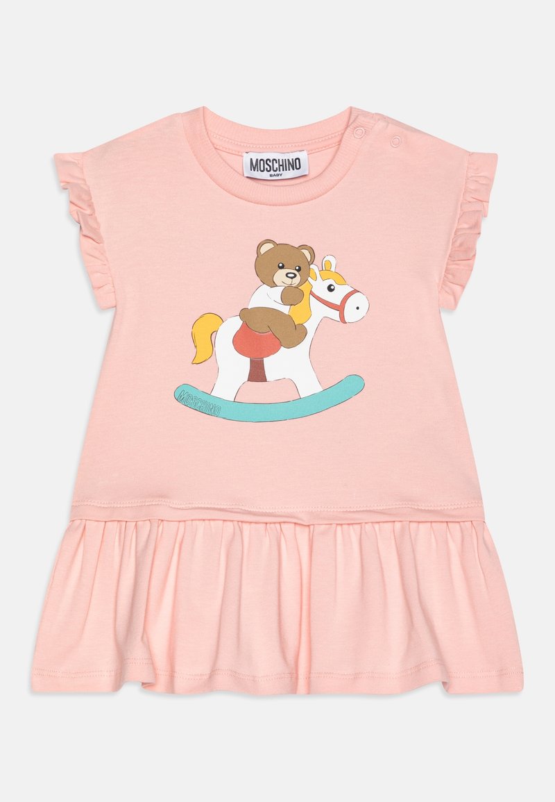 Vaaleanpunainen puuvillamekko, jossa on rypytetty hihansuut, kerääntynyt hame ja sarjakuvakarhu keinuvassa hevosessa -kuvio. Brändilogo, Moschino, näkyvissä.
