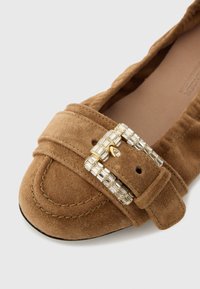 Rjav semiš raven čevelj z zaobljenim prstom, z okrasno zaponko z zlatim poudarkom in prozornimi kristali na zgornjem traku.