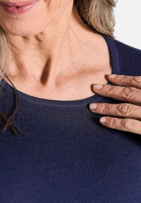 Dunkelblaues geripptes Strickoberteil mit Rundhalsausschnitt, das über einen strukturierten Stoff und eine figurbetonte Passform verfügt, teilweise auf Haut gezeigt.