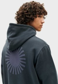 Donkergrijze hoodie met een grote cirkelvormige grafische print op de achterkant, met stralende lijnen. Katoenmengsel met een zachte textuur en een capuchon.