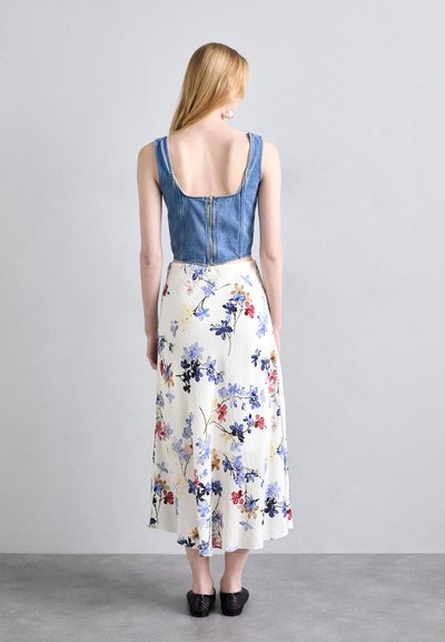 Denim crop top with wide straps and back zipper, paired with a flowy, knee-length white skirt featuring a colorful floral pattern.