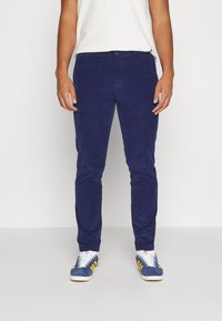 Námořnické kordové kalhoty s slim fit, mají knoflíkové zapínání a boční kapsy, kombinované s modrými teniskami a bílými ponožkami.