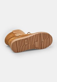 Stivale in suede beige con suola in gomma testurizzata, caratterizzato da un accento soffice sulla parte superiore e da lacci. La parte inferiore presenta un motivo scanalato per una migliore aderenza.