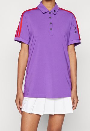Personne portant un polo violet avec des rayures rouges sur les manches et une jupe plissée blanche.