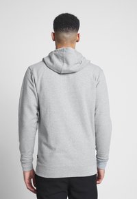 Sudadera con capucha gris de textura suave, con mangas largas, puños acanalados y un bolsillo tipo canguro. La vista trasera muestra el detalle de la capucha.