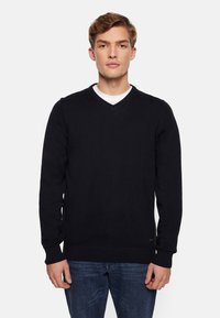 Czarny sweter knit z dekoltem w serek, z prążkowanymi mankietami i dołem. Nosi się go na białej koszuli, z małą etykietą marki na dole.