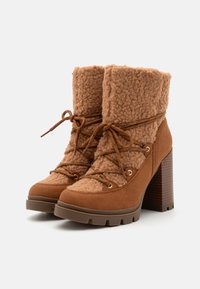 Brune hælede støvler med en fuzzy shearling-overdel og en ruskind-nederdel. Funktioner snørebåndsdesign, metaløjer og tekstureret blokhæl.