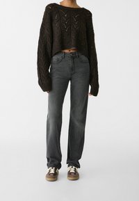 Suéter de punto marrón oscuro con un patrón de zigzag y diseño corto, combinado con jeans rectos gris y zapatillas marrones.