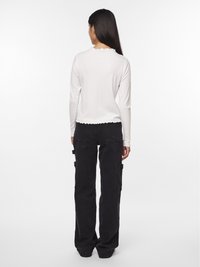 Biała bluzka z długim rękawem o prążkowanej fakturze i falbaniastym dołem, zestawiona z czarnymi spodniami cargo z dwoma bocznymi kieszeniami i luźnym krojem.