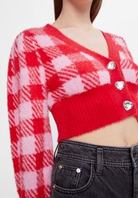 Cardigan corto rosso e rosa con motivo a quadri, scollo a v e tre bottoni a forma di cuore. Tessuto morbido e soffice, orlo a coste.
