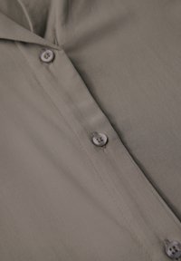 Camicia grigia con bottoni, realizzata in tessuto liscio con una leggera lucentezza. Presenta tre bottoni rotondi e un design del colletto.