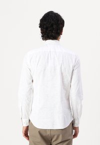 Cămașă albă cu mâneci lungi, cu un model subtil paisley, guler cu nasturi și tiv curbat. Textura materialului pare netedă și ușoară.