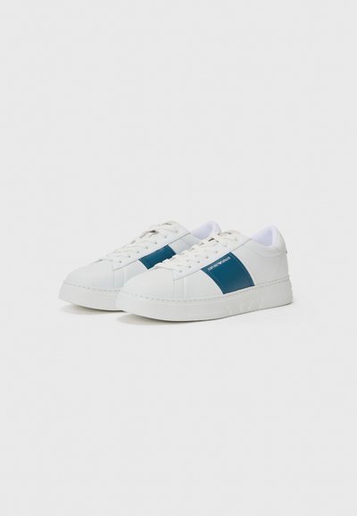 Vita sneakers med en blå sidopanel, tillverkade av glatt syntetmaterial. Har en texturerad gummisula och vita snören.