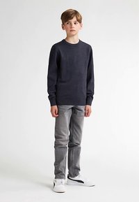 Pulover bleumarin închis, blugi gri conici și adidași albi. Puloverul are guler rotund și manșete ribbed. Textură netedă a țesăturii.