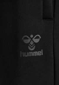 Zwarte stof met een gladde textuur, met een grijs Hummel-logo en een bijontwerp dat duidelijk zichtbaar is.