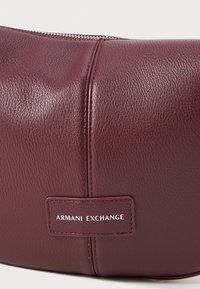 Burgunderfärgad läderhandväska med en texturerad yta, med en silverfärgad dragkedja och en präglad logotäcke. Slät, rund form.