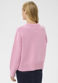 Pull rose tricoté avec un col et un ourlet côtelés, épaules tombantes et coupe décontractée. La texture semble douce et confortable.