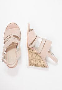 Roze suède sleehakken met open teenvorm. Voorzien van een gestructureerde kurken sleehak, elastische banden en een zilveren gesp.