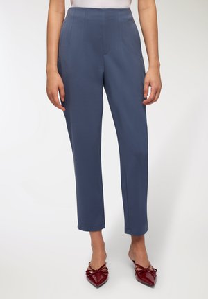 Pantaloni blu su misura con vita alta, gamba dritta e tasche laterali. Indossati con ballerine rosse lucide a punta con dettagli a fiocco.