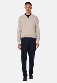 Beige pulóver na polovičný zips z mäkkej látky s golierom, kombinovaný s modrými plisovanými nohavicami a čiernymi teniskami, s minimalistickým dizajnom.