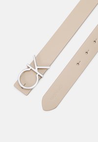 Beige leren band met een zilveren ronde gesp met een "OK" ontwerp. Inclusief verstelgaten voor maatvoering en een merkindruk.