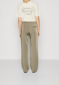 Lichtbeige t-shirt met de opdruk "Chelsea Racquet Club", gecombineerd met olijfgroene, wijde satijnen broek met een elastische tailleband en achterzak.