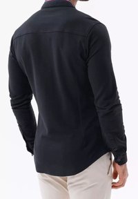 Maglietta nera a manica lunga con colletto, caratterizzata da una bordatura a contrasto, design aderente e polsini con bottoni. Tessuto liscio con una sottile texture.